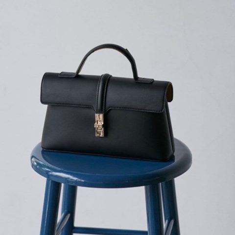 Sac à main noir à rabat et fermoir doré posé sur un tabouret